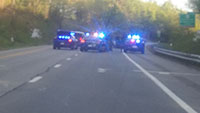 Blurry photo, police cars with lights flashing, one with open trunk. Officers standing and running on highway.