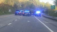 Blurry photo, police cars with lights flashing, one with open trunk. Officers standing and running on highway.